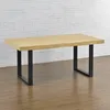 A wooden table with black metal legs is shown against a white brick wall and a wooden floor. Náhled obrázku produktu