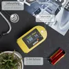 A yellow pulse oximeter is shown on a dark surface, with a stethoscope, a plant, and batteries nearby. Text overlays describe the product and its components. Produktbild-Vorschau