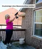 A woman is using a cordless pressure washer on the side of a brick house from a wooden deck. Produktbild-Vorschau