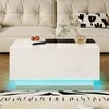A modern white coffee table with LED lighting is placed in a living room setting in front of a sofa. Podgląd zdjęcia produktu