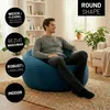 A man is sitting on a large blue beanbag chair in a living room. Produktbild-Vorschau