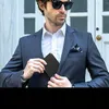 A man in a suit is putting a wallet into his jacket pocket. Anteprima dell’immagine prodotto