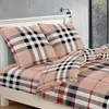 A close-up view of a bed with bedding featuring a plaid pattern. Produktbild-Vorschau