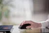 A hand using a black computer mouse next to a laptop. Voir les images du produit