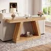 A wooden console table with a shelf is placed behind a sofa in a living room, with a lamp and decorative items on top and on the shelf. Podgląd zdjęcia produktu