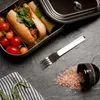 A stainless steel lunch box with sandwiches and cherry tomatoes, a fork, and a small bowl of pink salt on a dark surface. Podgląd zdjęcia produktu