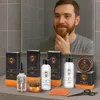A man is looking in the mirror at his beard, with a set of beard grooming products displayed on the counter in front of him. Náhled obrázku produktu