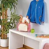 A children's backpack shaped like a horse sits on a white desk next to a green apple and a book. A blue jacket hangs on the wall behind it. Anteprima dell’immagine prodotto