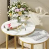 A set of two round nesting side tables with a marble-like finish and gold legs, decorated with a bouquet of flowers, books, and decorative deer figurines. Náhled obrázku produktu