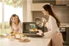 A mother and daughter are in a kitchen, with the mother taking a dish out of a microwave. Produktbild-Vorschau