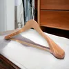 A wooden hanger is placed on a white cloth surface inside a closet, with clothes visible in the background and wooden drawers to the right. Produktbild-Vorschau
