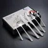 A set of silverware is displayed on a black surface, with the product box in the background. Podgląd zdjęcia produktu