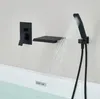 A black built-in bathtub faucet with a waterfall spout and a handheld showerhead is shown mounted on a wall above a bathtub filled with water. Podgląd zdjęcia produktu
