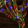 Close-up of colorful LED string lights wrapped around tree branches at night. Produktbild-Vorschau