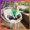 A woman is sitting in a white hanging chair on a balcony with plants in the background. Náhled obrázku produktu