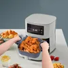 A person is holding a silicone insert filled with fried chicken next to an air fryer. There are also croissants and strawberries visible. Produktbild-Vorschau
