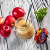 A jar of applesauce with apples and a spoon on a wooden table. Podgląd zdjęcia produktu