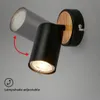 A black adjustable wall lamp with a wood accent, mounted on a gray wall. Produktbild-Vorschau