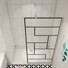 A modern bathroom with white tiled walls and a patterned floor, featuring a glass shower enclosure with a black frame. Produktbild-Vorschau
