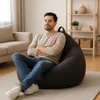 A man is sitting on a beanbag chair in a living room. Voir les images du produit