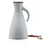 A light gray insulated carafe with a black lid and a curved handle sits on a white surface. A small pile of coffee beans is scattered to the right of the carafe. Voir les images du produit