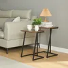 Two C-shaped side tables with walnut-colored tops and black metal frames are placed next to a light-colored sofa. One table holds a small plant in a white geometric pot and a white mug. The other table has two books and a small wooden lamp. Podgląd zdjęcia produktu