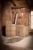 Two cardboard boxes are placed on a concrete floor in what appears to be a construction or unfinished space. There is a puddle of water on the floor. Podgląd zdjęcia produktu