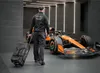 A person walks away from a Formula 1 car, pulling a rolling bag. Produktbild-Vorschau