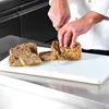 A chef is slicing a loaf of bread on a white cutting board. Voir les images du produit