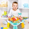 A baby is playing with an interactive music table in a room with shelves filled with toys. Produktbild-Vorschau