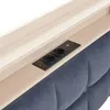 A close-up view of a wooden shelf integrated into a dark gray tufted headboard, featuring a black electrical outlet and USB port. Podgląd zdjęcia produktu