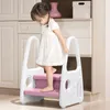 A young girl is standing on a pink and white step stool. Voir les images du produit