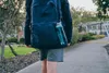 A person wearing a backpack with a water bottle attached is walking on a sidewalk. Anteprima dell’immagine prodotto