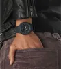 A close-up shot of a person's wrist wearing a black watch, with their hand in the pocket of brown corduroy pants. The person is also wearing a black leather jacket. Voir les images du produit