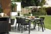 An outdoor dining set with chairs and a table on a patio, with a garden in the background. Náhled obrázku produktu