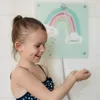A young girl in a swimsuit is playing with water in her hands, with a rainbow-themed decoration on the wall behind her. Anteprima dell’immagine prodotto
