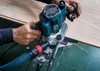 A person is using a router on a wooden surface, with a dust collection hose attached. Produktbild-Vorschau