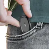 A hand is placing a small black electronic device into the pocket of a pair of jeans. Produktbild-Vorschau