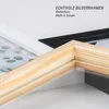 A close-up view of the corner of three picture frames, one natural wood, one white, and one black, with text overlay. Produktbild-Vorschau