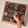 A hand holding a small jar in front of an advent calendar. Produktbild-Vorschau