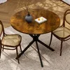 A round dining table with two chairs on a patterned rug, with a vase of flowers and two oranges on the table. Produktbild-Vorschau