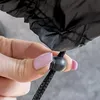 A close-up of a hand holding a drawstring toggle on a black fabric item. Náhľad obrázku produktu