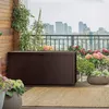 A brown storage box on a balcony with plants and a city skyline in the background. Podgląd zdjęcia produktu