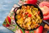 A close-up of a dish of cooked vegetables in a pan, with images of tomatoes in the background. Produktbild-Vorschau
