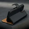 A black leather iPhone wallet case with a brown interior is shown standing upright on a dark surface. Produktbild-Vorschau