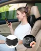 A woman is sitting in a car and using her phone, with a massage pillow attached to the headrest. Produktbild-Vorschau