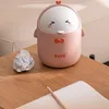 A cute cartoon duck-shaped trash can is placed on a wooden table next to a crumpled piece of paper and a notebook with a pencil. Produktbild-Vorschau