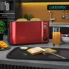 A red toaster with bread inside, placed on a kitchen counter with a glass of orange juice and berries nearby. Produktbild-Vorschau