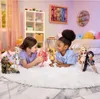 Two young girls are lying on a fluffy white rug, playing with several fashion dolls in a brightly lit room. Anteprima dell’immagine prodotto