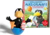 A toy figure of the character Rabe Socke sitting in a blue base, next to a book with the same character on the cover. Produktbild-Vorschau
